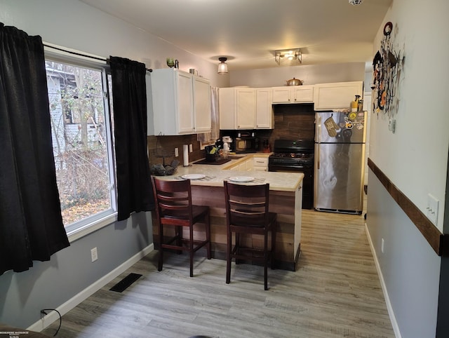 kitchen with white cabinets, black gas range, stainless steel refrigerator, and plenty of natural light