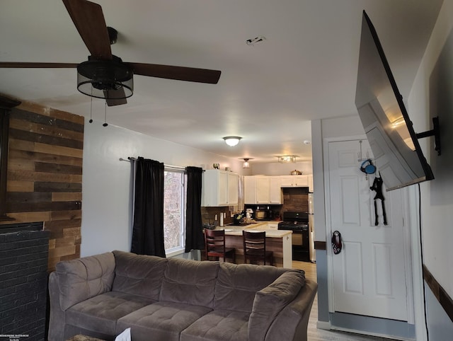 living room with ceiling fan, light wood-type flooring, and wooden walls