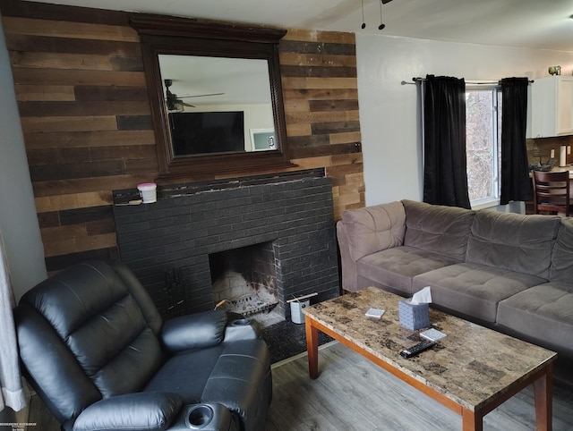 living room featuring hardwood / wood-style floors, ceiling fan, wooden walls, and a brick fireplace