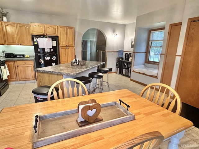 kitchen with black appliances, a kitchen island, light tile patterned flooring, and a breakfast bar area