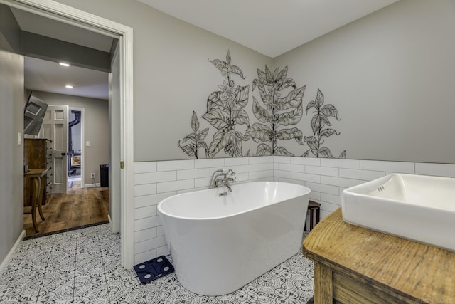 bathroom featuring a tub to relax in, tile patterned flooring, tile walls, and sink