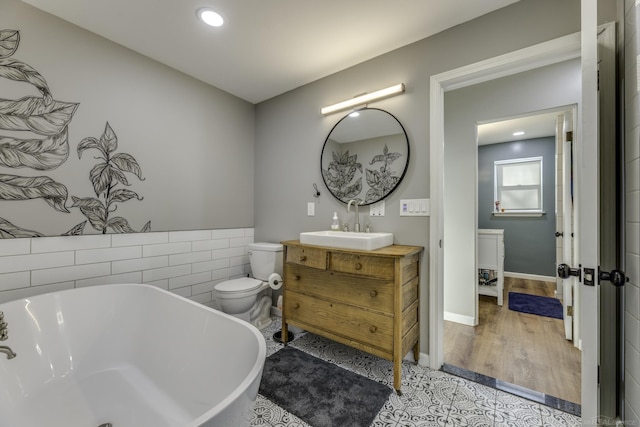 bathroom with a tub to relax in, toilet, vanity, tile walls, and hardwood / wood-style flooring