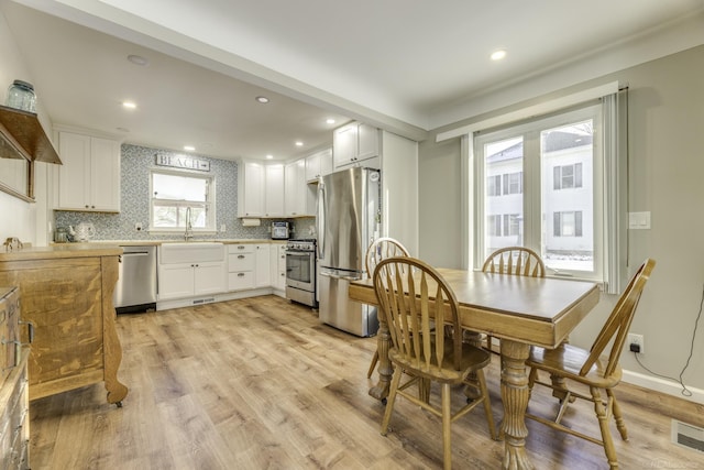 kitchen with white cabinetry, sink, decorative backsplash, appliances with stainless steel finishes, and light wood-type flooring