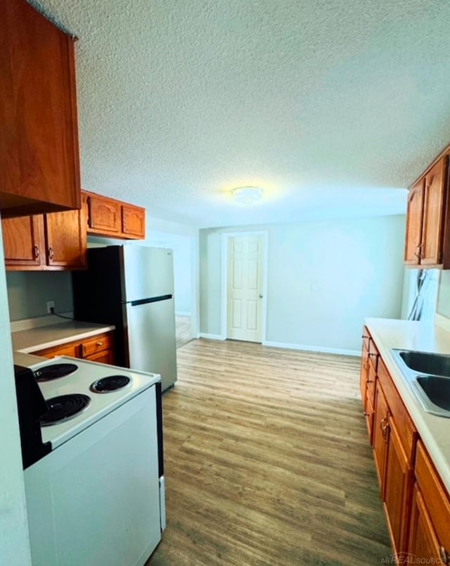 kitchen with sink, light hardwood / wood-style flooring, stainless steel refrigerator, electric range, and a textured ceiling