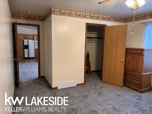 unfurnished bedroom featuring carpet, a closet, ceiling fan, and fridge with ice dispenser