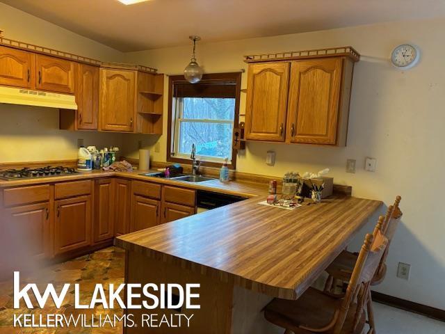 kitchen featuring decorative light fixtures, vaulted ceiling, kitchen peninsula, sink, and stainless steel gas cooktop