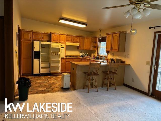 kitchen with lofted ceiling, kitchen peninsula, a kitchen bar, sink, and fridge with ice dispenser