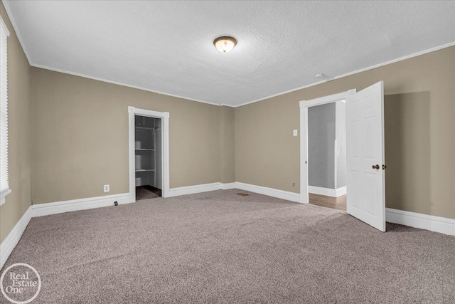 unfurnished bedroom with ornamental molding, a textured ceiling, a spacious closet, carpet floors, and a closet