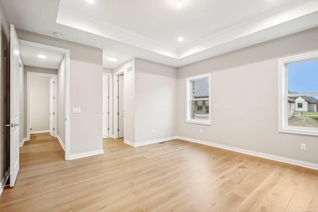 empty room with light wood-type flooring and a tray ceiling