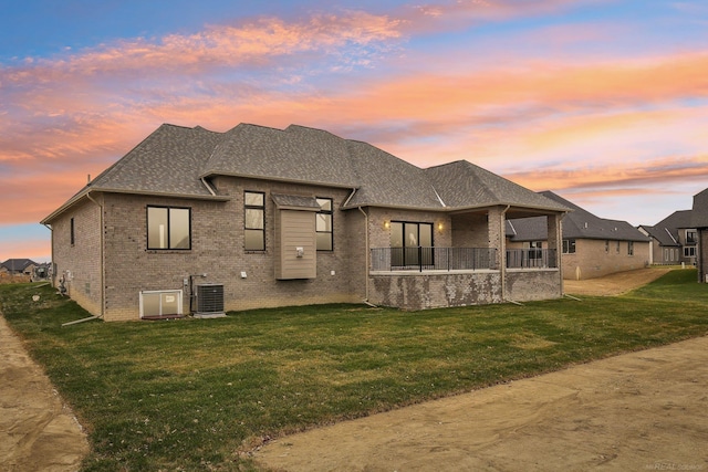 back house at dusk with a yard and central AC unit