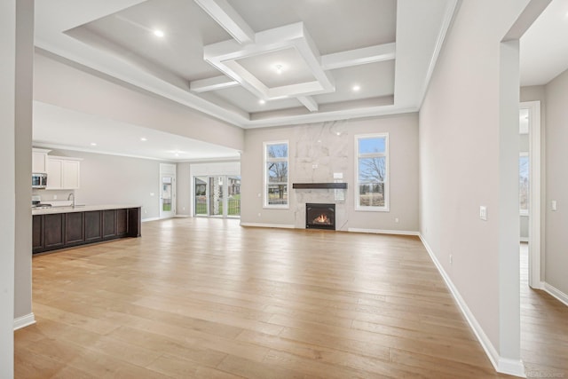 unfurnished living room with coffered ceiling, a large fireplace, beam ceiling, and light hardwood / wood-style flooring