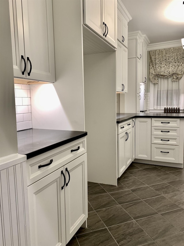 kitchen with white cabinets, dark tile patterned floors, ornamental molding, and backsplash