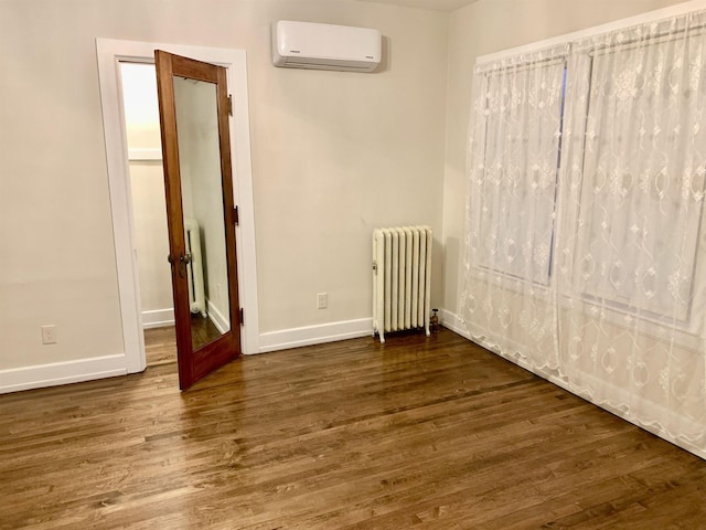 empty room featuring radiator heating unit, dark wood-type flooring, and an AC wall unit