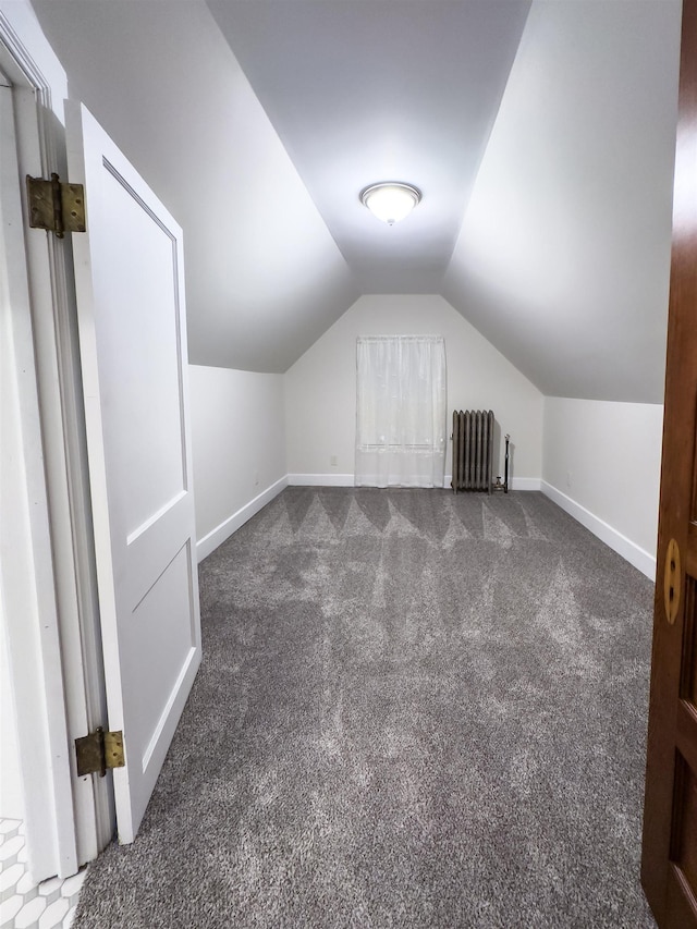 bonus room featuring dark colored carpet, radiator heating unit, and vaulted ceiling