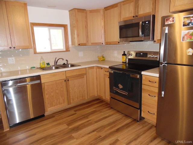 kitchen with backsplash, sink, stainless steel appliances, and light hardwood / wood-style floors