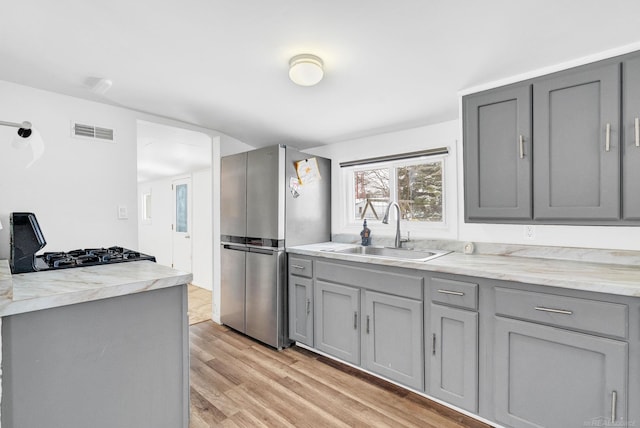 kitchen featuring stainless steel fridge, light wood-type flooring, gray cabinetry, and sink