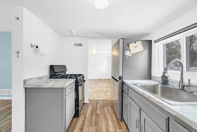 kitchen with gray cabinetry, black gas range, sink, light hardwood / wood-style flooring, and stainless steel refrigerator