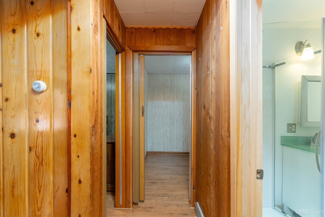 corridor with light wood finished floors and wooden walls