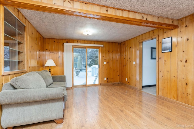 living area featuring wooden walls, a textured ceiling, baseboards, and wood finished floors