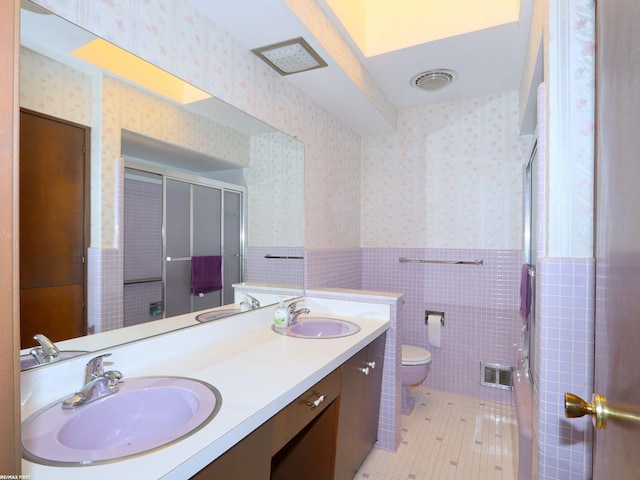 bathroom with walk in shower, tile patterned flooring, toilet, vanity, and tile walls