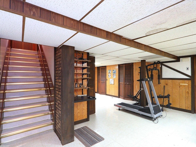 exercise room with a drop ceiling and wood walls