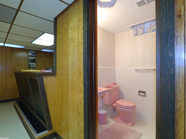 bathroom featuring a paneled ceiling, toilet, and wood walls