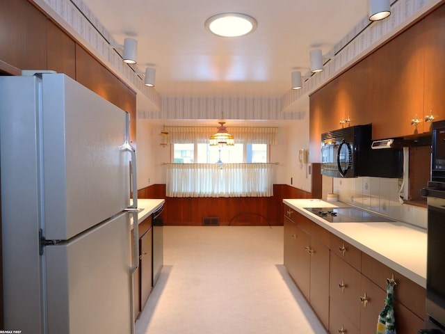 kitchen featuring pendant lighting, light carpet, black appliances, wooden walls, and tasteful backsplash