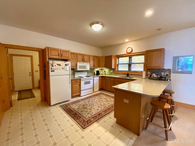 kitchen with kitchen peninsula, tasteful backsplash, a breakfast bar, white appliances, and sink