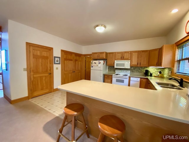 kitchen with sink, backsplash, kitchen peninsula, white appliances, and a kitchen bar