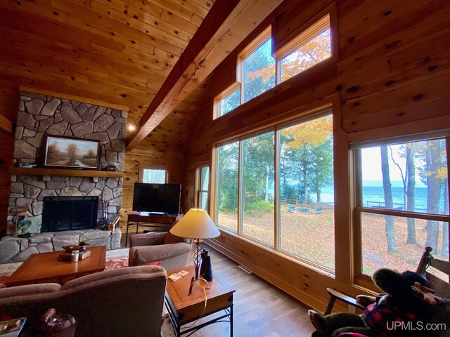 living room featuring a stone fireplace, wooden walls, lofted ceiling with beams, and light wood-type flooring