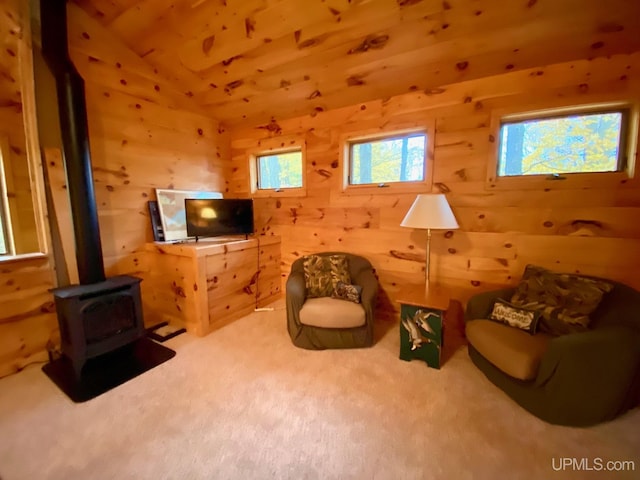 sitting room with a wood stove, wooden walls, carpet, and vaulted ceiling