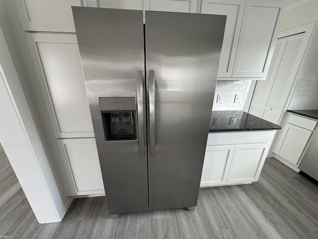 kitchen featuring stainless steel refrigerator with ice dispenser, backsplash, dark stone counters, light hardwood / wood-style floors, and white cabinets