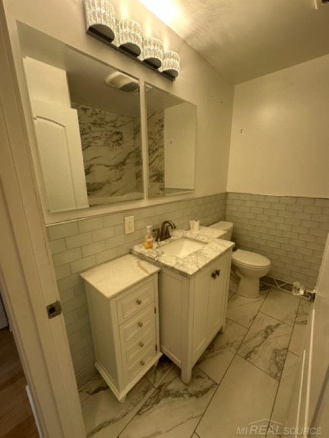 bathroom featuring vanity, tile walls, and toilet