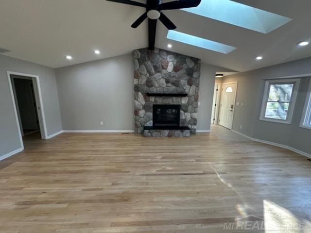 unfurnished living room featuring a fireplace, ceiling fan, vaulted ceiling with skylight, and light wood-type flooring