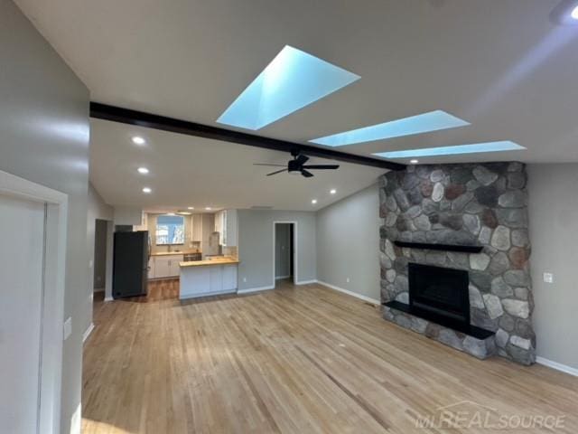 unfurnished living room with a skylight, a stone fireplace, ceiling fan, and light hardwood / wood-style floors