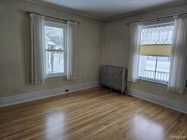 empty room featuring light hardwood / wood-style floors, ornamental molding, and radiator