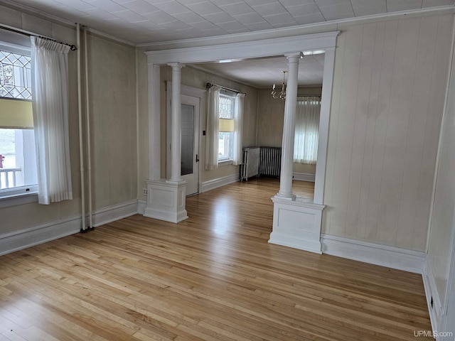 unfurnished room featuring radiator, wood walls, light hardwood / wood-style flooring, and a notable chandelier