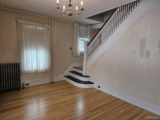 interior space with radiator, hardwood / wood-style flooring, a notable chandelier, wooden walls, and ornamental molding