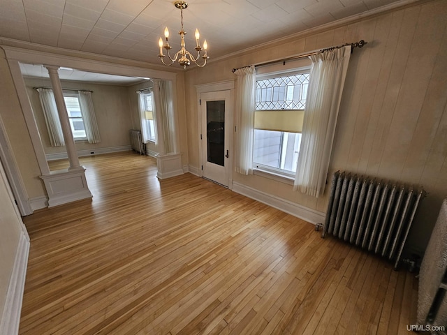 empty room with ornate columns, a chandelier, radiator heating unit, and light hardwood / wood-style floors