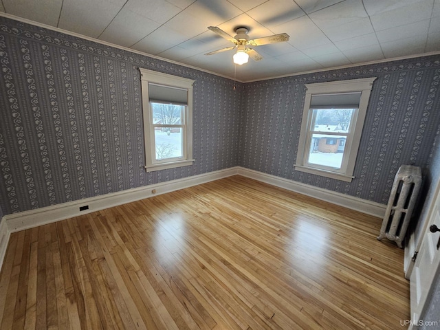 empty room featuring wood-type flooring, plenty of natural light, radiator, and ceiling fan