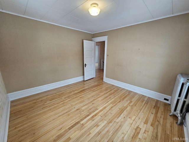 empty room with radiator heating unit, light hardwood / wood-style floors, and ornamental molding