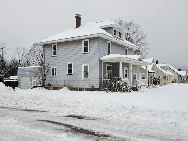 snow covered property featuring a porch, a garage, and an outbuilding