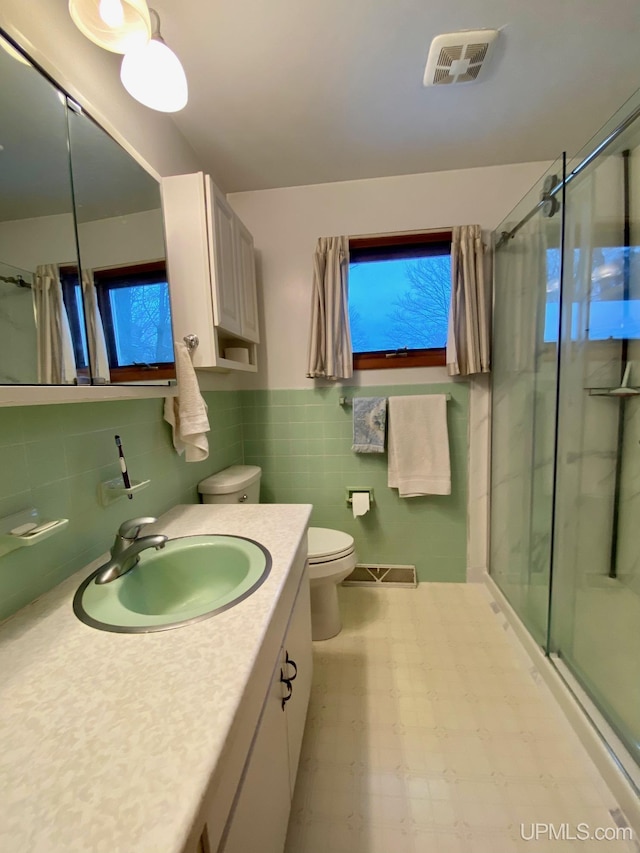 bathroom with an enclosed shower, vanity, toilet, and tile walls