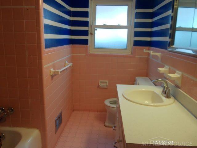 bathroom with vanity, toilet, and tile walls