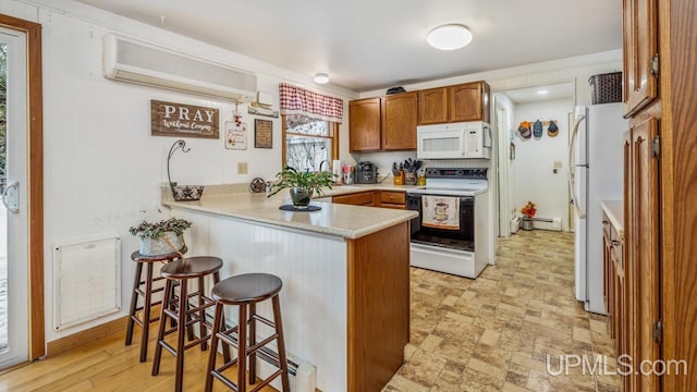 kitchen featuring baseboard heating, kitchen peninsula, a wall mounted AC, white appliances, and a kitchen bar