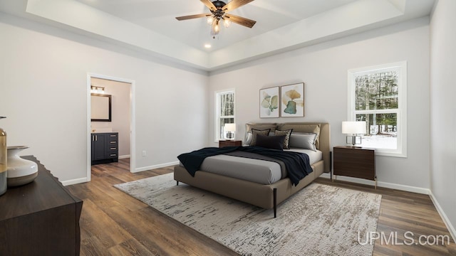 bedroom featuring ceiling fan, dark hardwood / wood-style floors, a tray ceiling, and connected bathroom