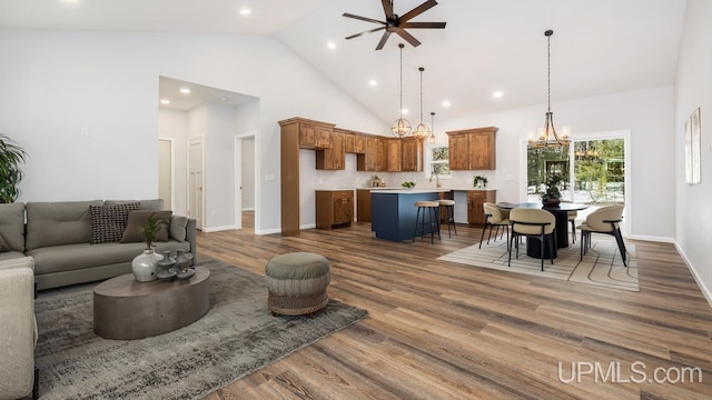 living room featuring dark hardwood / wood-style flooring, ceiling fan with notable chandelier, and high vaulted ceiling