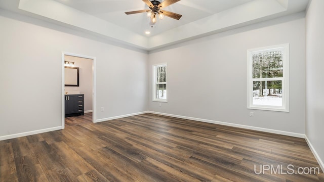 empty room featuring dark hardwood / wood-style floors, ceiling fan, and a raised ceiling