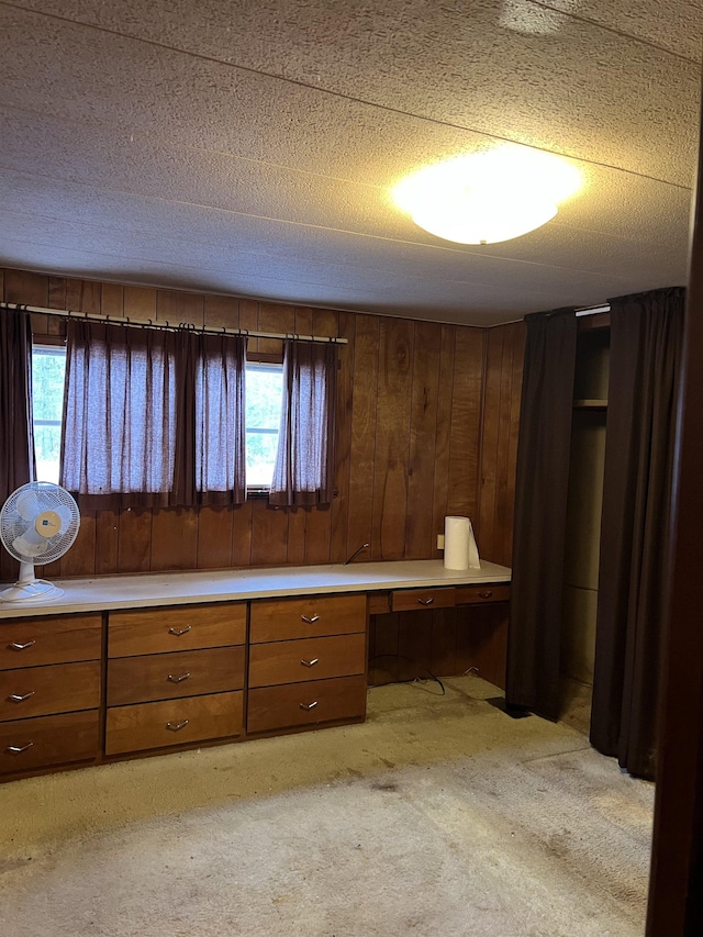 unfurnished bedroom with a textured ceiling, built in desk, light colored carpet, and multiple windows