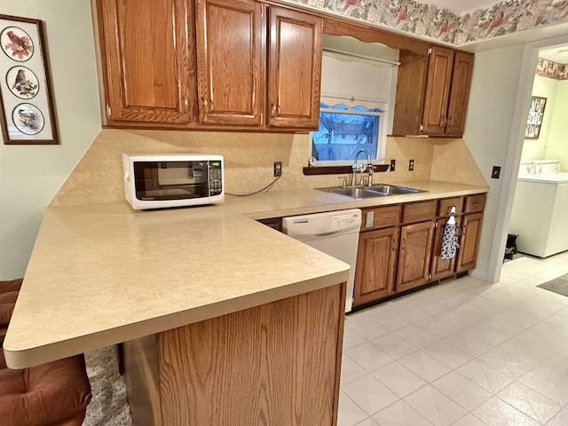 kitchen with kitchen peninsula, washer / dryer, white appliances, and sink